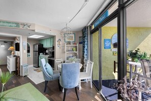 A modern kitchen with a refrigerator, stove, and dining area with chairs and a table. - Jaw-Dropping Ocean View King Ste w/Breakfast (Myrtle Beach)