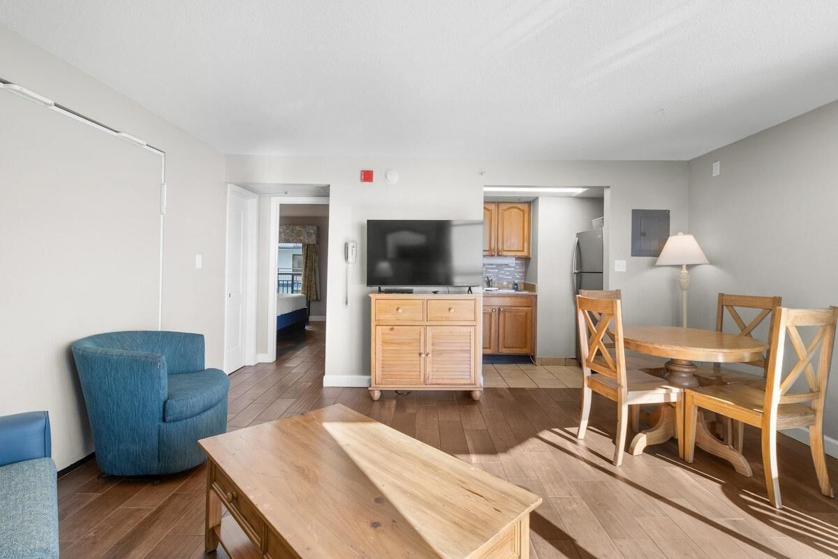 A spacious living area with a wooden dining table, blue armchairs, and a kitchen in the background.