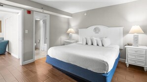 Ein Schlafzimmer mit einem großen Bett, zwei Nachttischen, einem Beistelltisch, einem Sessel und einer Tür zu einem anderen Raum.