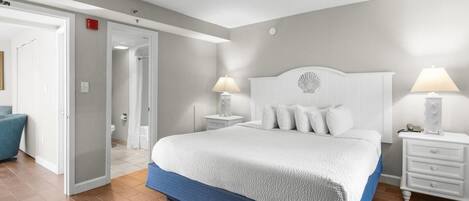 A bedroom with a large bed, two bedside tables, a nightstand, a chair, and a door leading to another room.