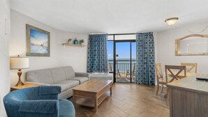 A living room with a sofa, a coffee table, and a dining area with chairs. - Mesmerizing Ocean View King Ste: Breakfast 14th Fl (Myrtle Beach)