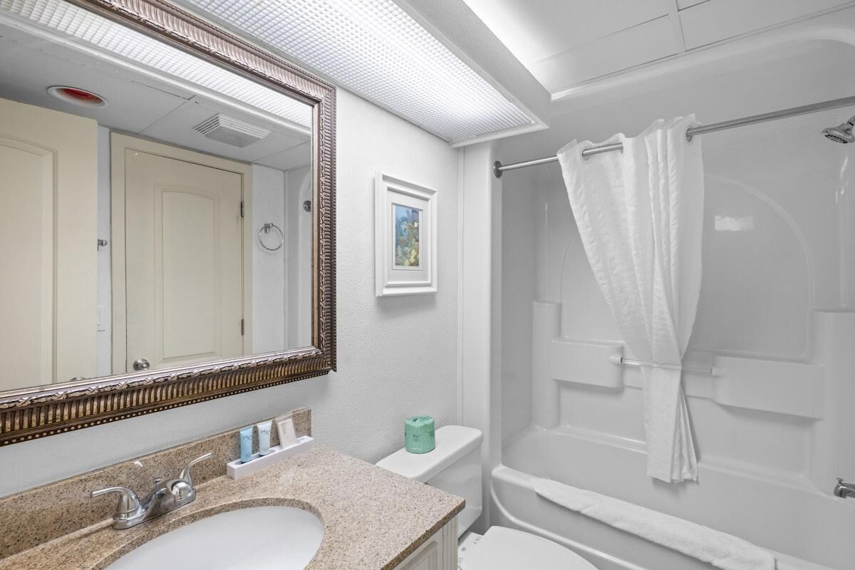 A bathroom with a sink, mirror, toilet, and shower.