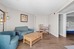 A modern living room with a blue sofa, a wooden coffee table, and a dining area with a table and chairs. - Majestic Ocean View Ste: Free Breakfast 11th Flr (Myrtle Beach)