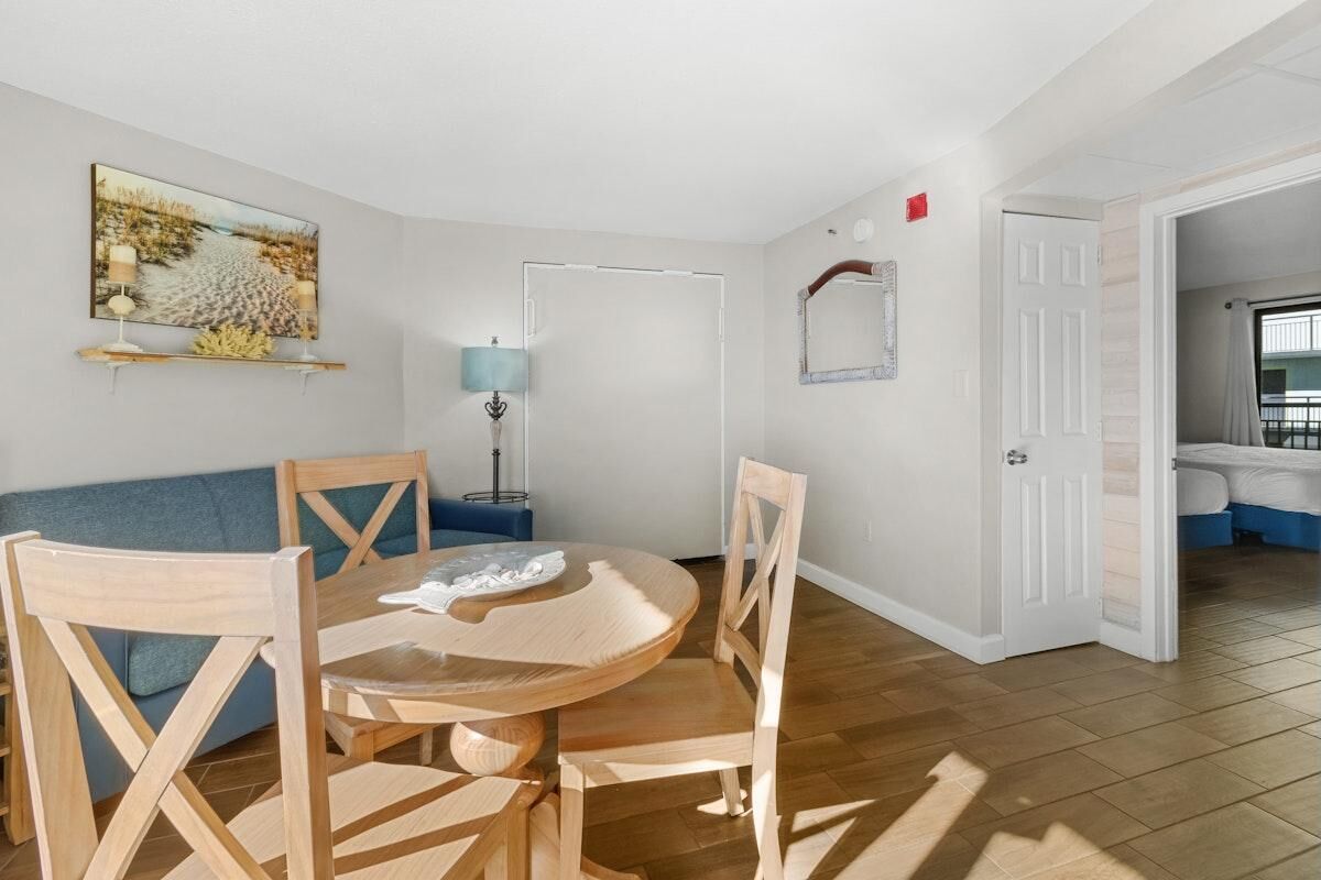 A room with a round wooden table, two chairs, a blue sofa, a lamp, and a painting on the wall.