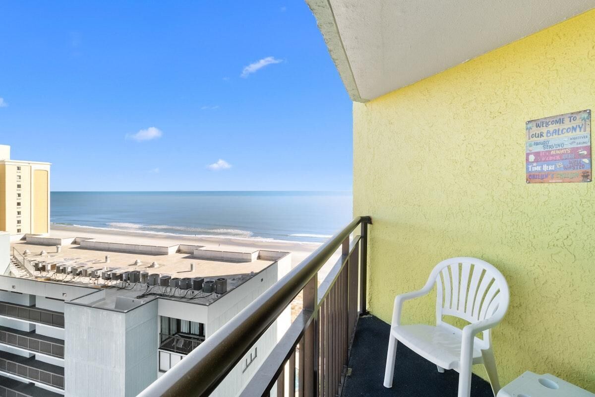 Een balkon met uitzicht op het strand en de oceaan, een witte plastic stoel, en een bord aan de muur.