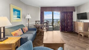 A living room with a sofa, a coffee table, a TV, and a balcony with curtains. - Inspiring Ocean View Ste Free Breakfast 12th Flr (Myrtle Beach)