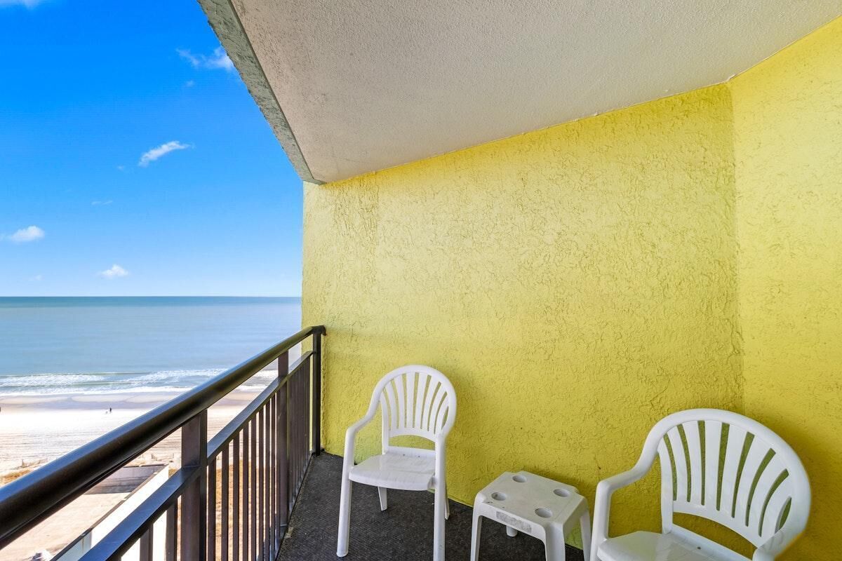 A balcony with a yellow wall, two white chairs, and a small table.