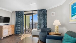 Una sala de estar moderna con una televisión de pantalla plana, un mueble de madera, un sillón azul, un cojín azul verdoso y una lámpara sobre una mesita.