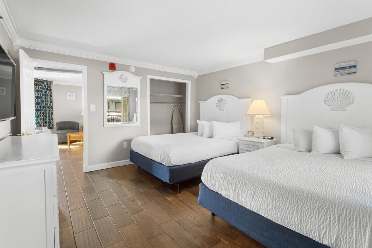 A hotel room with two beds, a wardrobe, a vanity, and a bathroom.