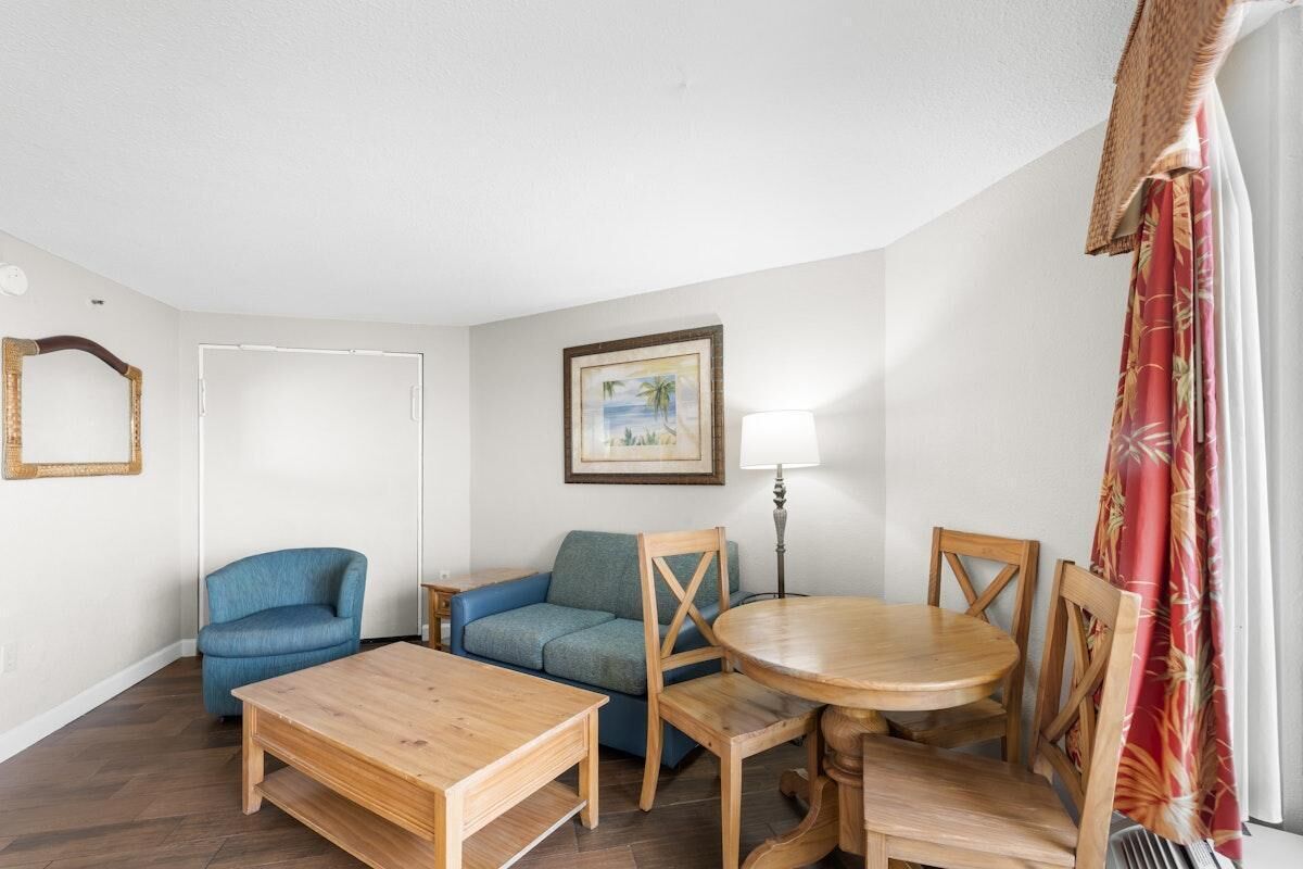 A living room with a wooden table, two blue chairs, a sofa, and a lamp.