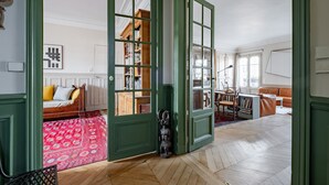 A spacious room with a large open door leading to another area, a wooden bed, a red patterned rug, and a bookshelf. - Marais Melody, by Veeve (Paris)