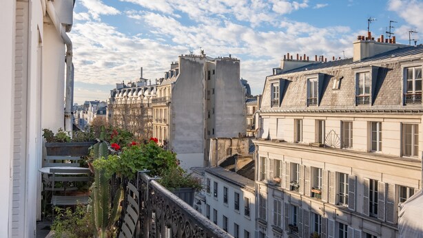 A view of a cityscape with buildings, a balcony with plants, and a clear sky. - Marais Melody, by Veeve (Paris)