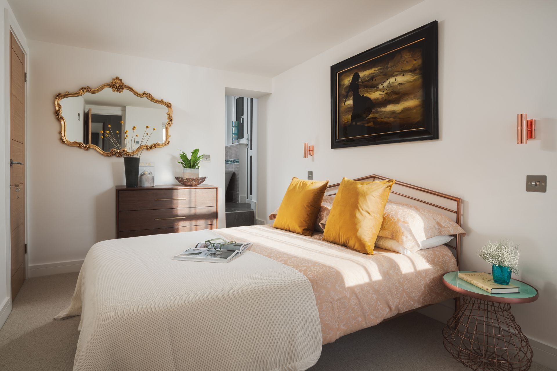 A bedroom with a bed, a dresser, a mirror, a painting, and a small table with a plant.