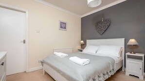 A bedroom with a bed, bedside tables, a white dresser, a radiator, and a heart-shaped wall decoration. - Kinnessburn Road Apartment (No 20) (St Andrews)