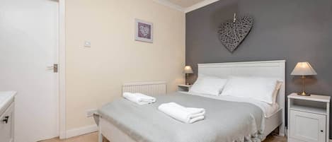 A bedroom with a bed, bedside tables, a white dresser, a radiator, and a heart-shaped wall decoration.