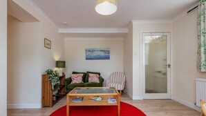 A living room with a red carpet, a green sofa, a striped armchair, a wooden coffee table, and a painting on the wall. - Kinnessburn Road Apartment (No 20) (St Andrews)
