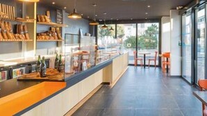 A modern cafe with a long counter, shelves with baked goods, and a view through large windows. - Maison 6pers 1,2km de la Plage Smarttv Fibre (Les Sables-d'Olonne)