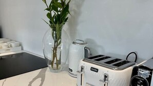 Ett kök med en vit bänkskiva, en brödrost, en kaffebryggare och en vas med gröna växter.