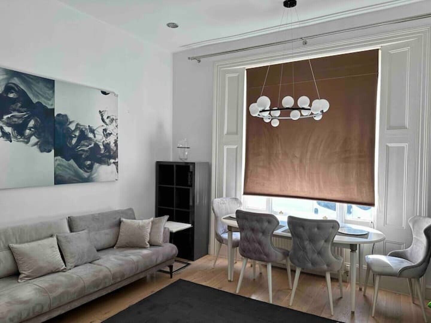 A modern living room with a grey sofa, a dining table with chairs, and abstract wall art.