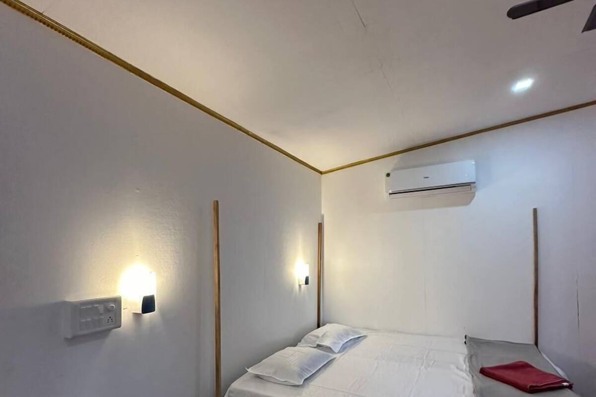 Um quarto pequeno e bem iluminado, com uma cama de casal, um aparelho de ar condicionado e um ventilador de teto.