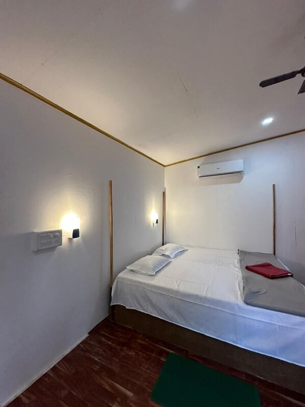 A small, well-lit bedroom with a single bed, an air conditioning unit, and a ceiling fan.