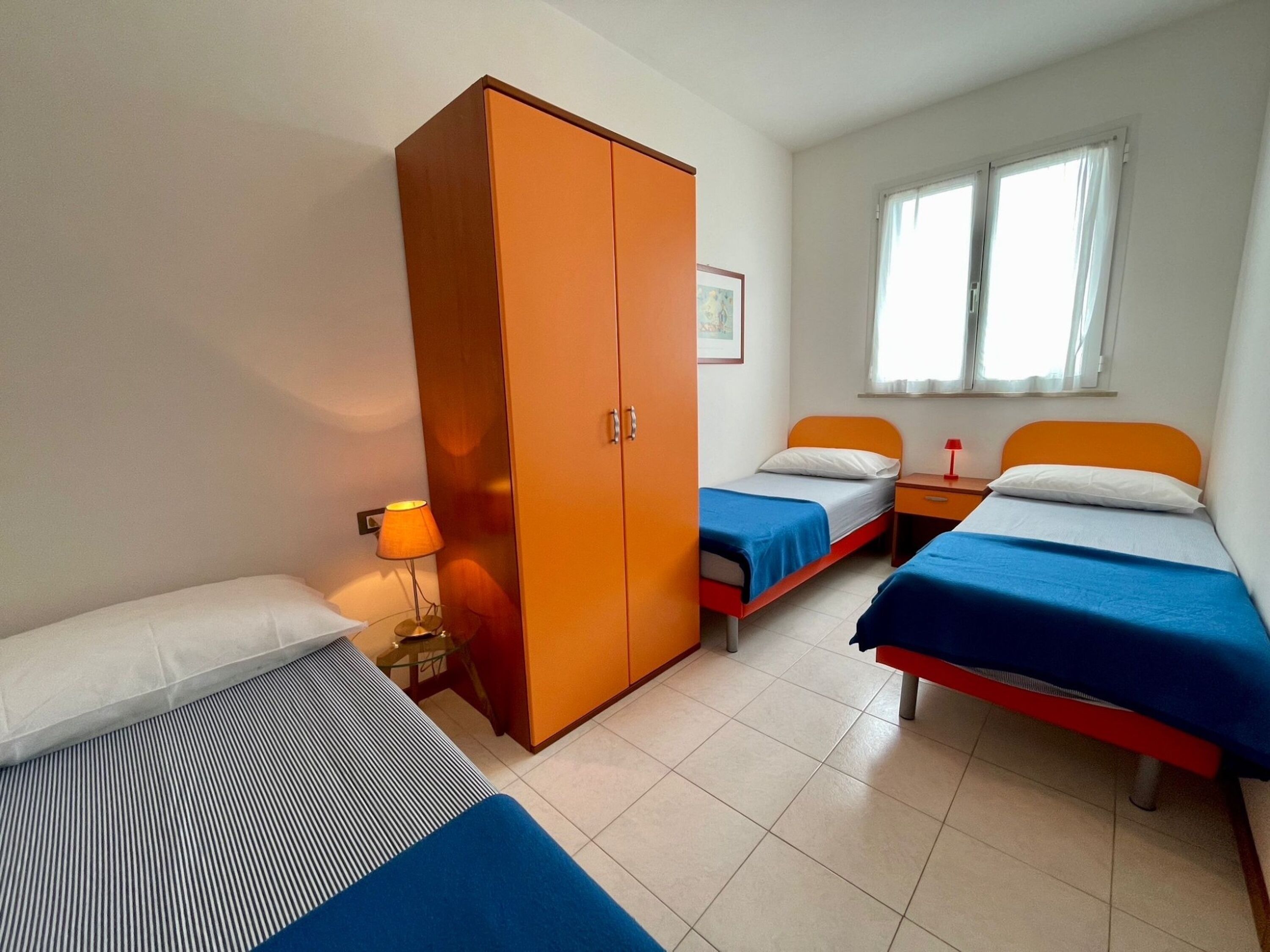 Une chambre avec deux lits, une armoire, une lampe et une fenêtre.