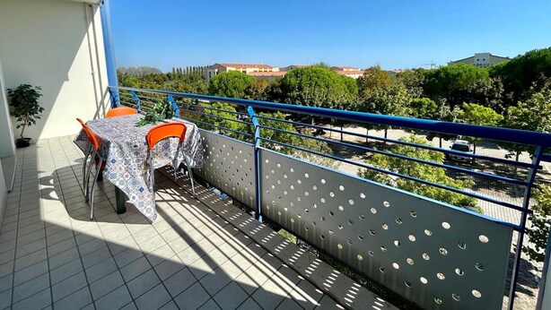 A balcony with a table and chairs, a view of trees and buildings, and a blue railing. - Luminous Flat With Balcony (Caorle)