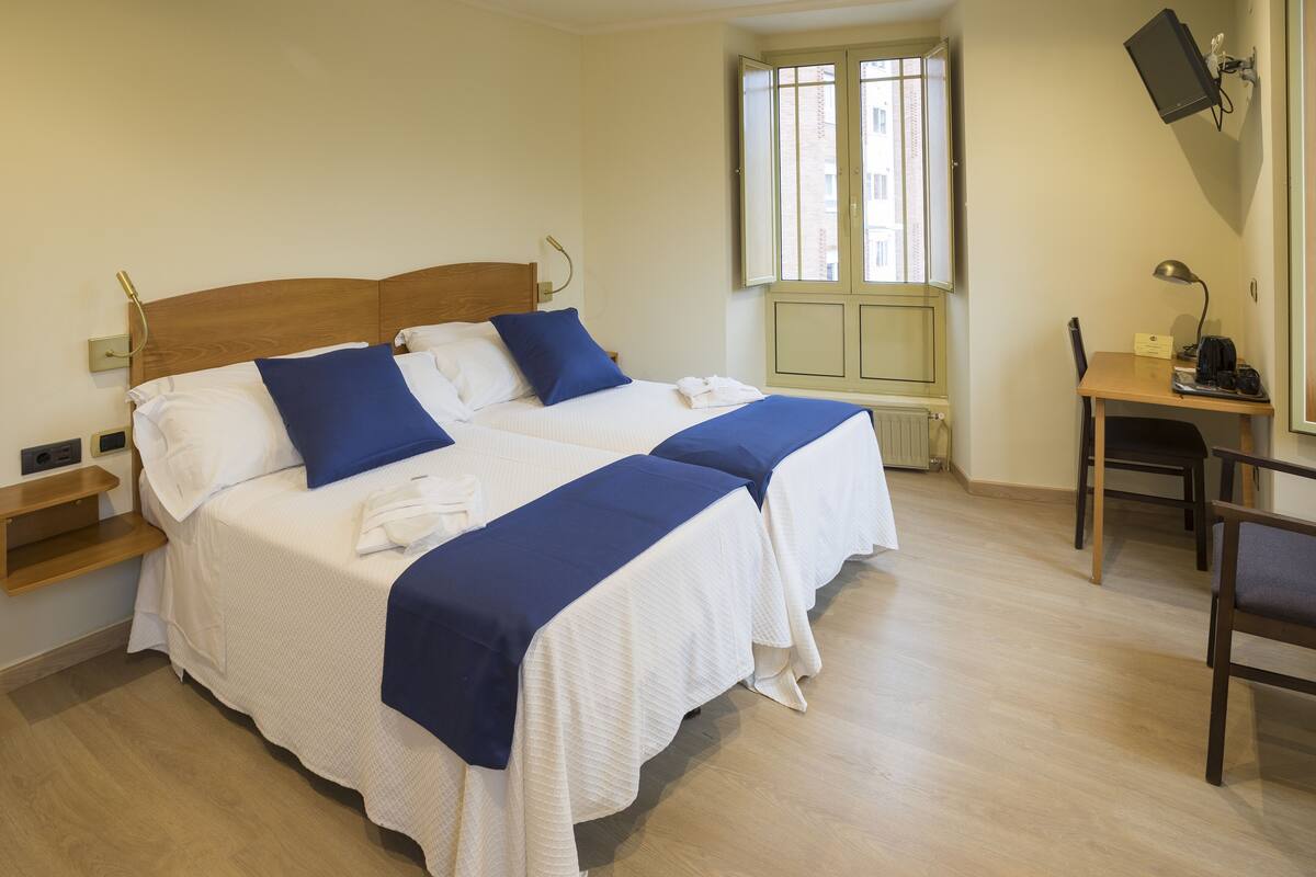 A double bed with white and blue bedding, a wooden headboard, and a bedside table with a lamp.
