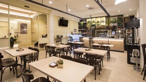 Un restaurante con varias mesas y sillas, una zona de bar con estantes llenos de botellas y un televisor colgado en la pared.