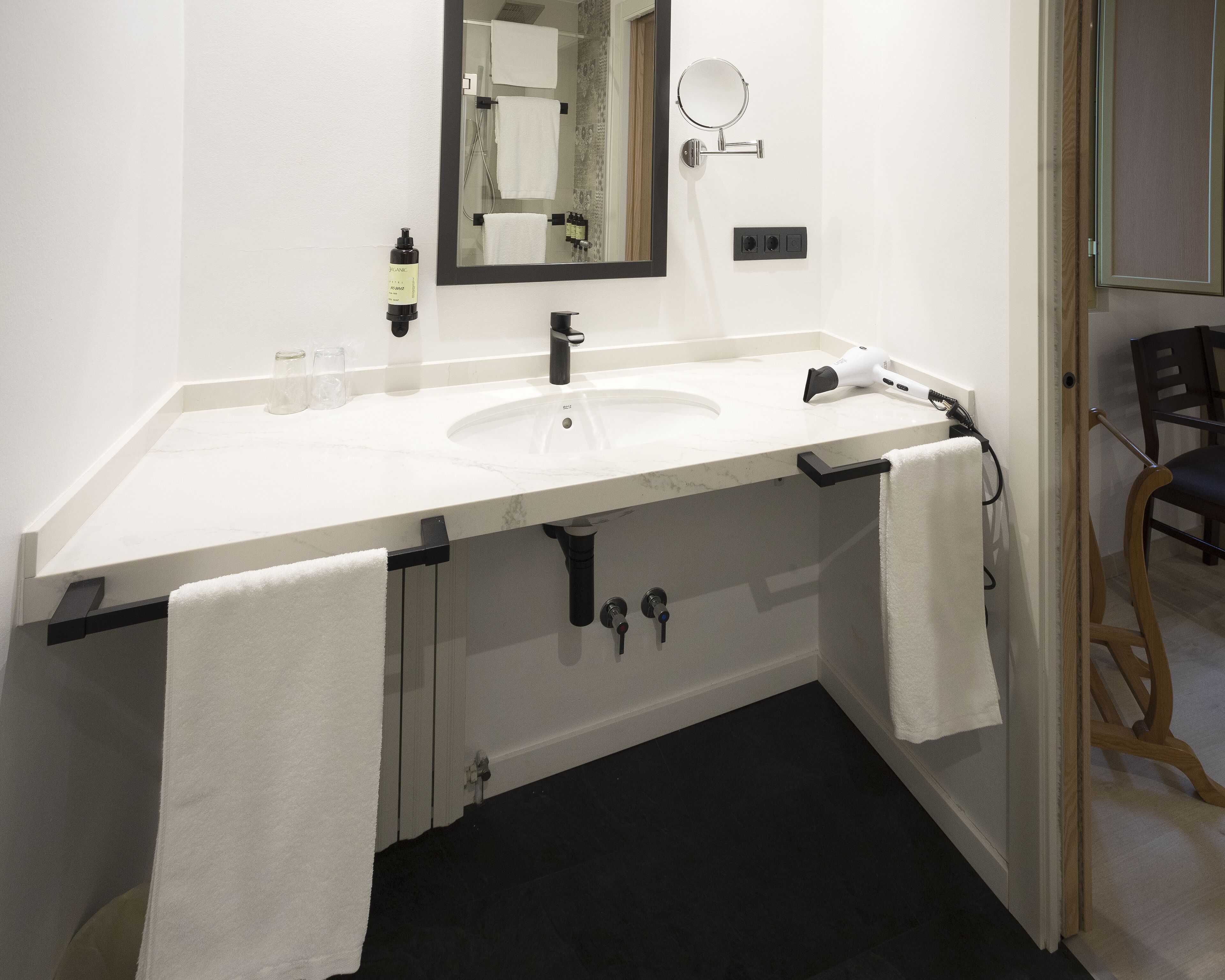 Un baño moderno con un lavamanos blanco, un espejo y un perchero para toallas.