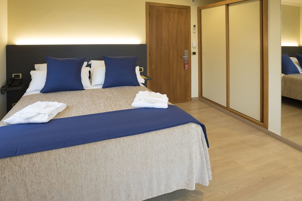 A neatly made bed with a blue and white bedspread, a wooden headboard, and a wooden floor.
