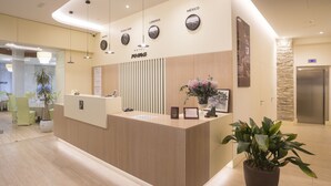 Un mostrador de recepción de hotel con detalles de madera, un reloj que marca la hora y un cartel con el nombre del hotel.