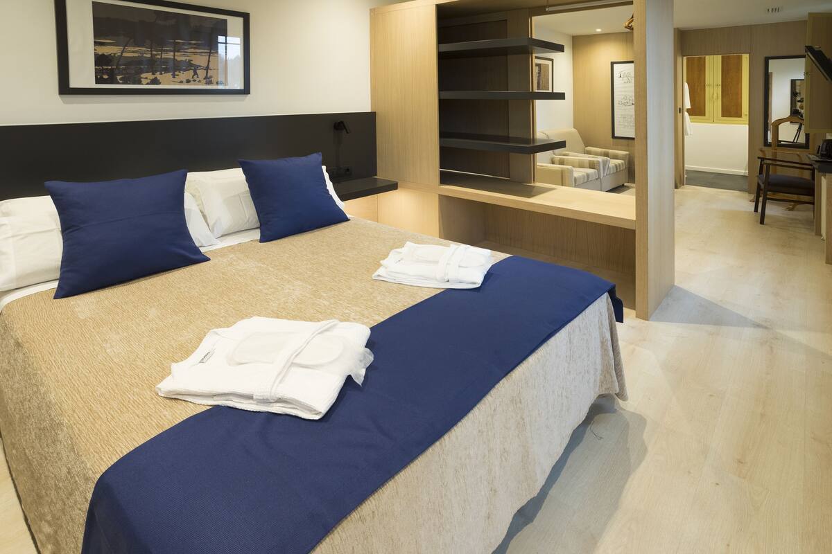 A neatly made bed with blue and white bedding, a bedside table, and a wall-mounted shelf.