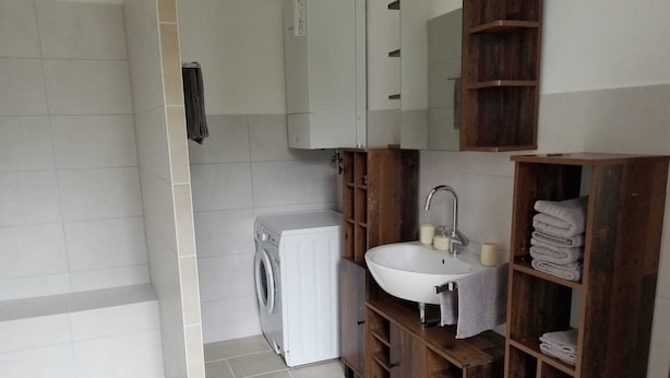 A compact bathroom with a washing machine, a sink, and wooden shelves. - Gemütliches 2-zimmer Appartement im Herzen von Lahnstein (Lahnstein)