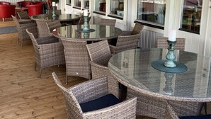 Ein Restaurant mit Korbmöbeln, Glastischen und großen Fenstern.