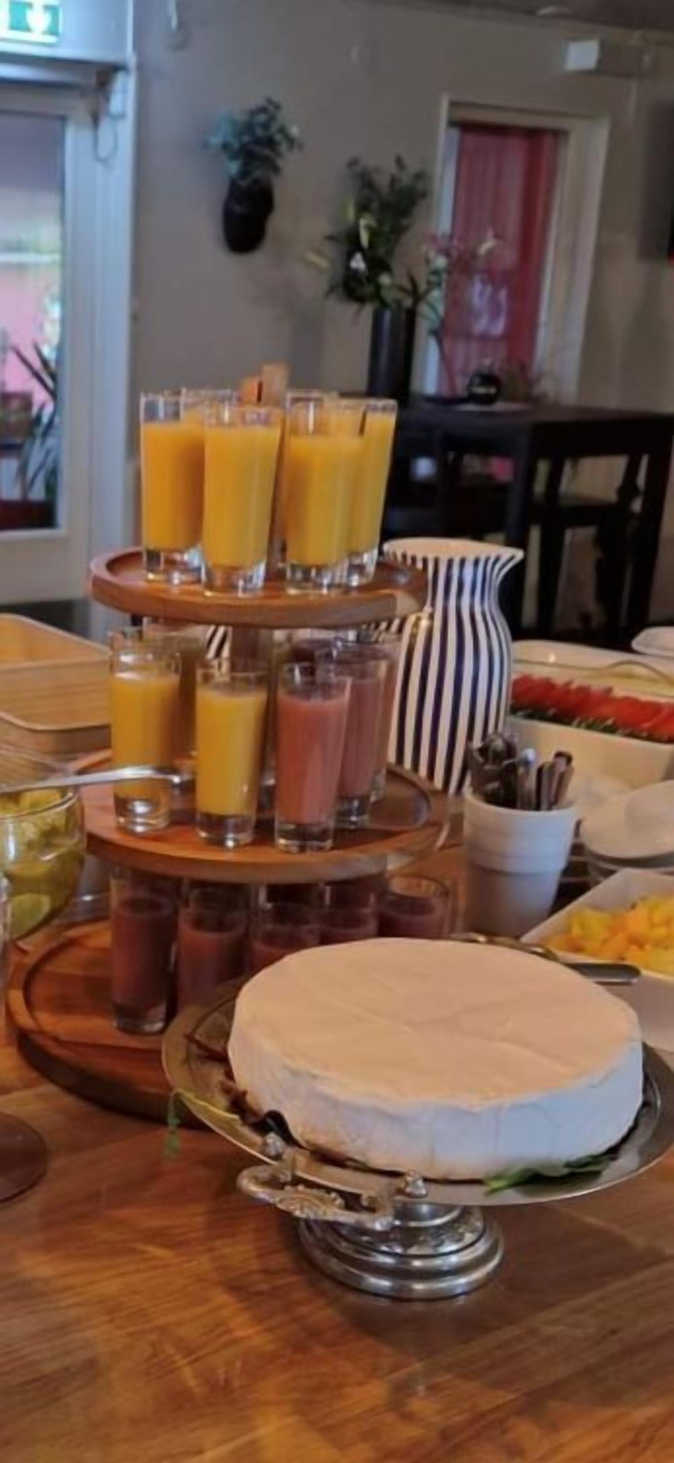 En frukostbuffé med olika sorters juice, en kanna och en kaka på ett träbord.