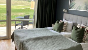 Ein Schlafzimmer mit Bett, Stuhl, Tisch und Blick auf einen Golfplatz durch eine Glastür.