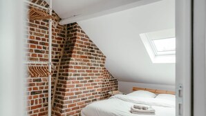 A bedroom with a sloped ceiling, exposed brick wall, wooden bed frame, and a skylight. - Duplex 4pers - 100m du Métro - Smarttv - Fibre (Lille)