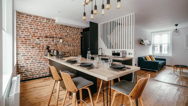 A modern kitchen with a brick wall, wooden bar stools, and pendant lighting. - Duplex 4pers - 100m du Métro - Smarttv - Fibre (Lille)