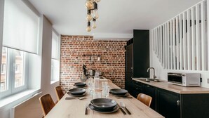 A modern kitchen with a brick wall, wooden dining table, and black cabinets. - Duplex 4pers - 100m du Métro - Smarttv - Fibre (Lille)