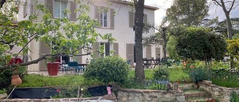 A villa with a stone wall, a garden with various plants, and outdoor furniture.