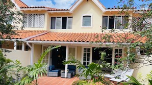 A two-story house with a tiled roof, a covered patio with outdoor seating, and a garden with various plants. - Stylish, light villa w/pool. All modern amenities, gated. Right by the beach. (Rodney Bay)