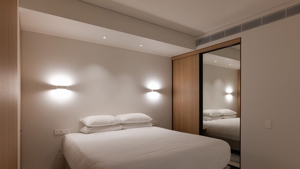 A modern bedroom with a large bed, two wall-mounted lights, and a full-length mirror. - City Living at it's Finest (Sydney)