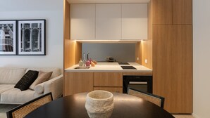 A modern kitchen with wooden cabinets, a built-in oven, and a dining area with a table and chairs. - City Living at it's Finest (Sydney)