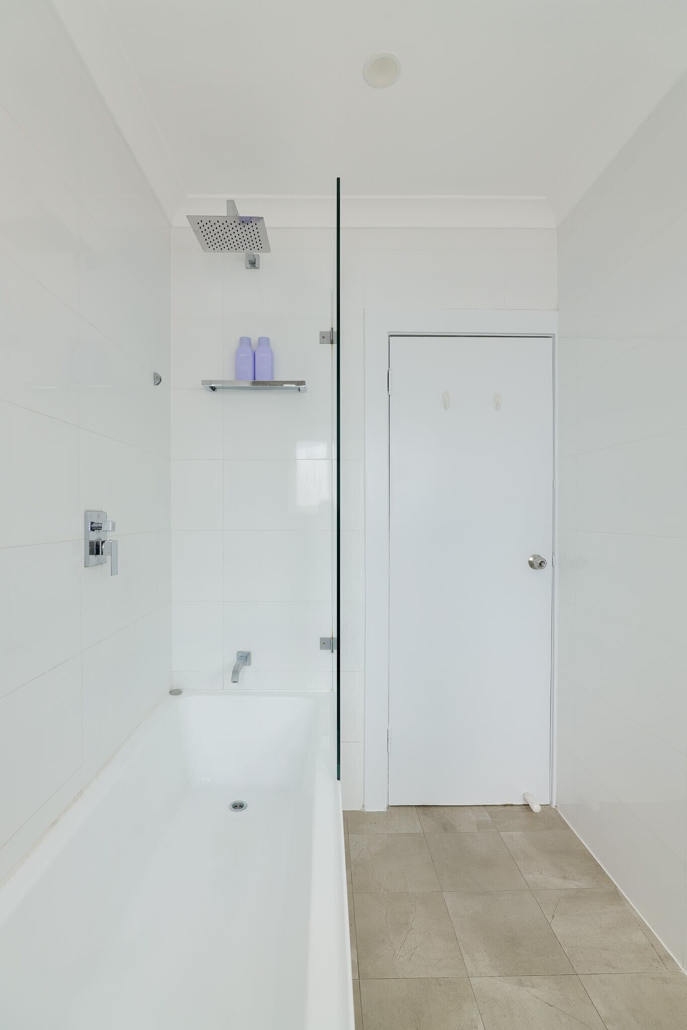 A modern bathroom with a white bathtub, a showerhead, and a door.