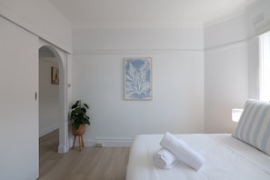 A minimalist hotel room with a bed, a framed artwork, a potted plant, and a view of a cityscape. - Bondi Beachfront Bliss (Bondi Beach)