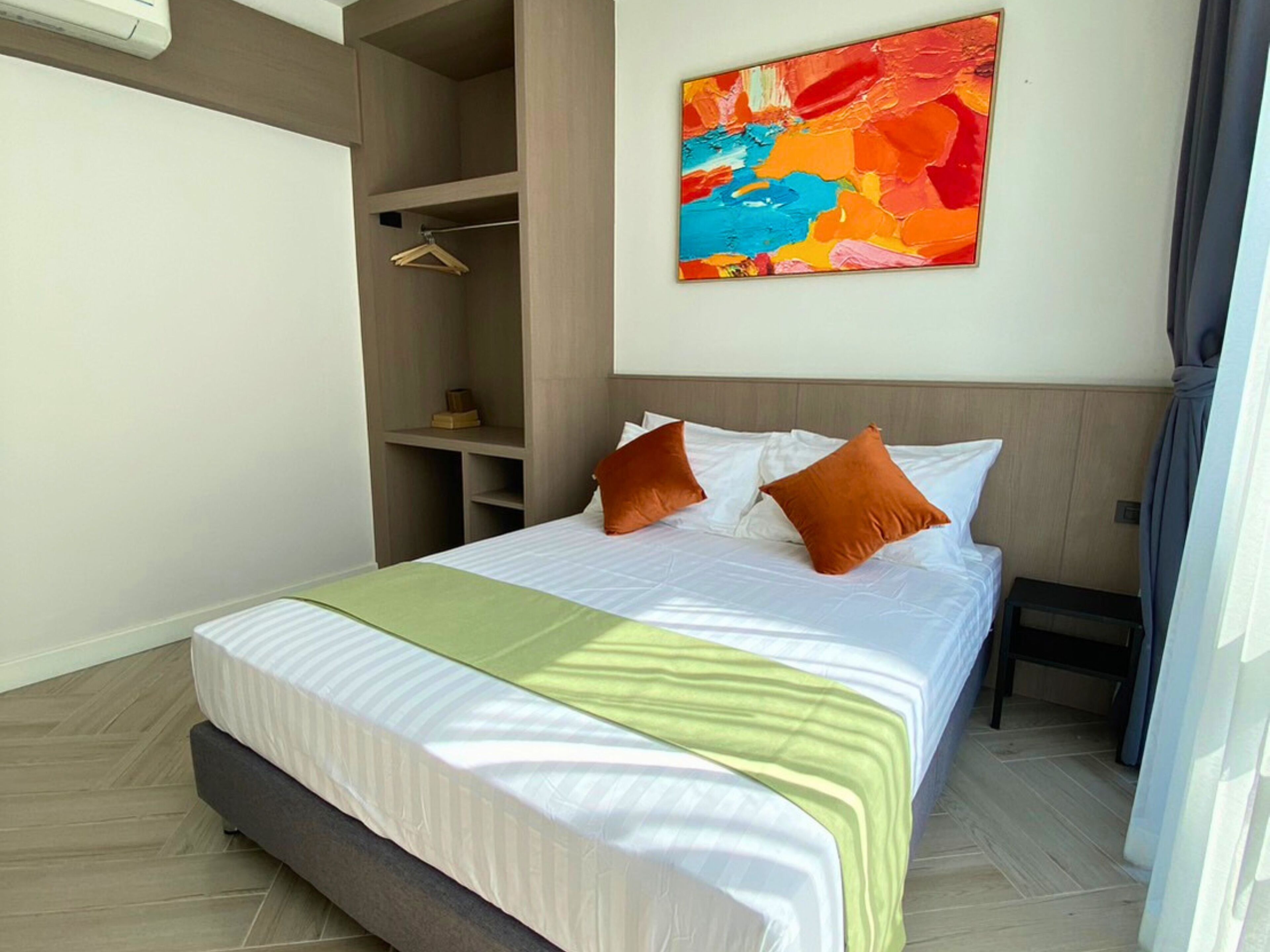 A hotel room with a bed, a wardrobe, and a colorful abstract painting on the wall.