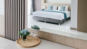 A modern hotel room with a large bed, a view of the ocean, and a wooden side table with a vase of flowers. - Sand Dance Hotel (Prachuap Khiri Khan)