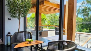 A modern outdoor seating area with a table and two chairs, a potted plant, and a view of a pool and greenery. - Sand Dance Hotel (Prachuap Khiri Khan)