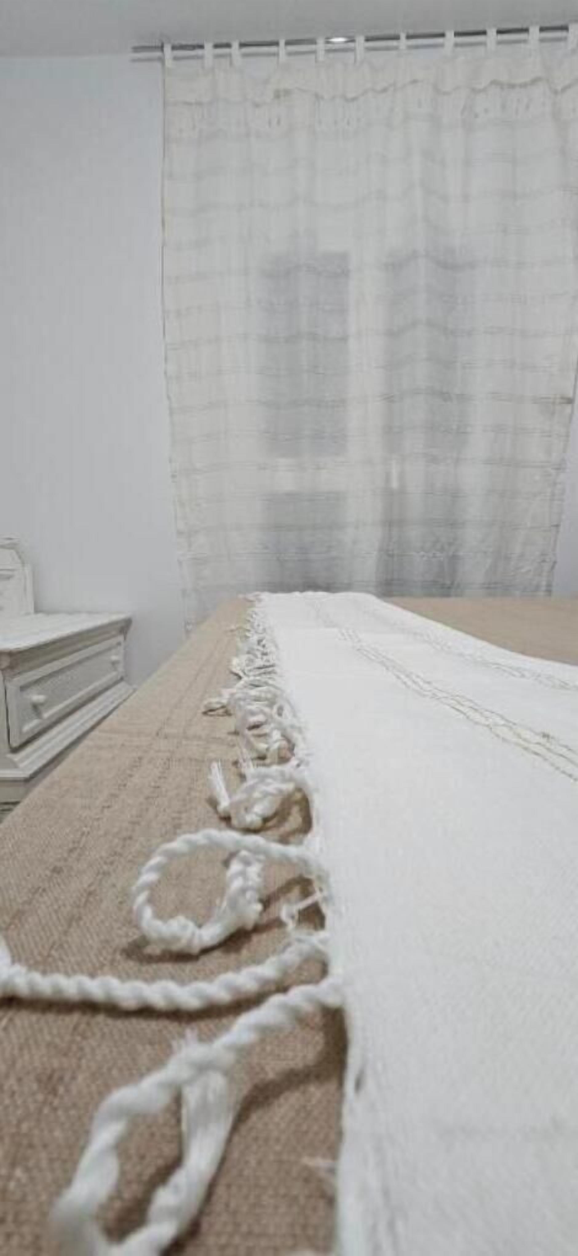 Une chambre avec un lit, une tête de lit blanche et une fenêtre avec un rideau blanc.